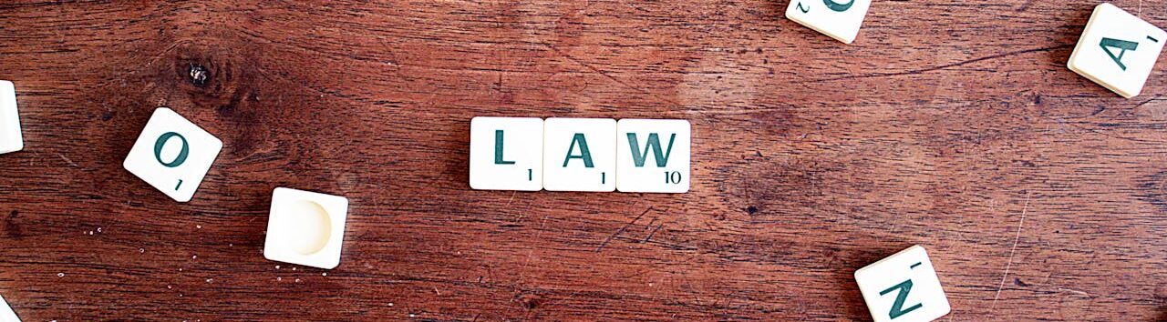Scrabble tiles spelling LAW on a wooden table, symbolizing connections to education and legality.